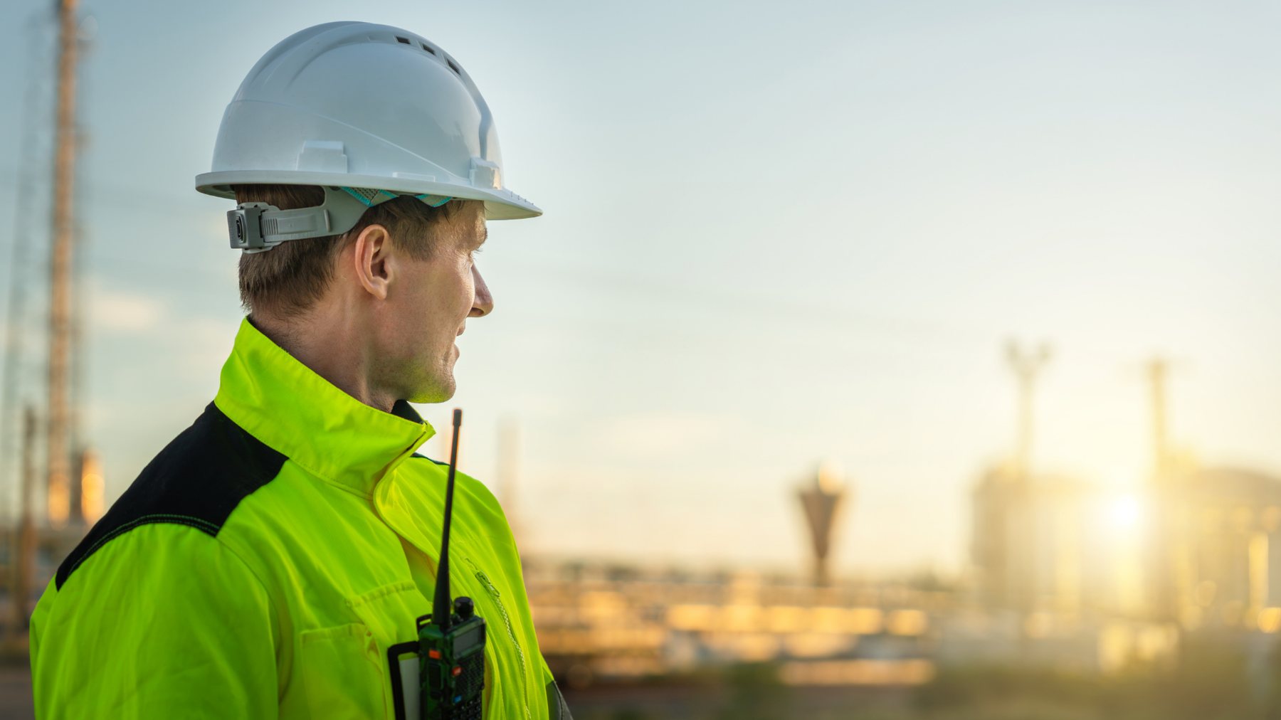 Técnico com rádio a observar uma instalação industrial ao entardecer